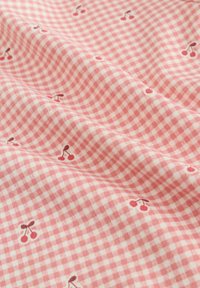 Rózsaszín és fehér kockás szöveten apró piros cseresznyeminták, amelyek lágy redőkön szóródnak szét.