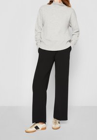 Jasnoszary sweter z wysokim kołnierzem, zestawiony z czarnymi spodniami o szerokich nogawkach oraz kremowymi sneakersami z czarnymi akcentami i brązowymi podeszwami.