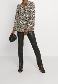 Blus med leopardmönster, lång ärm, v-ringning och volangmanschetter, kombinerad med högmidjade svarta läderbyxor med slitsar, och svarta nätklackar.