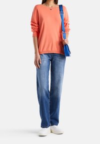 Korálový svetr, volný střih, žebrovaný lem; světle modré džíny, rovný střih; bílé tenisky; modrá crossbody taška s nastavitelným popruhem.