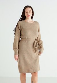 Vestido de punto beige con mangas largas, cuello redondo y cintura ceñida con cinturón. Presenta un acabado texturizado y un ligero canalé en toda su superficie.