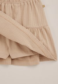 Jupe texturée beige avec taille élastique superposée à un short assorti, montrant les détails du tissu et les coutures intérieures sur un fond neutre.