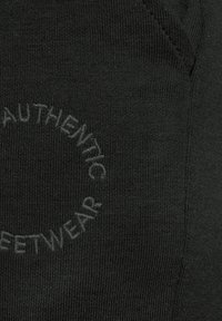 Czarna dzianina ma tłoczone okrągłe logo z napisem "AUTENTYCZNY STREETWEAR". Tekstura jest prążkowana z równomiernymi liniami.