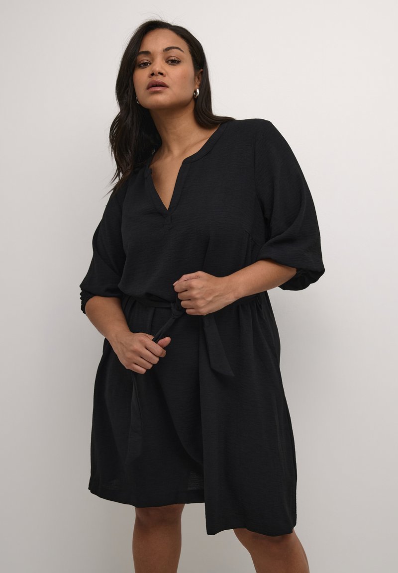 Robe noire à mi-mollet en tissu léger, avec un décolleté en V, des manches trois-quarts et une ceinture à nouer à la taille. Texture lisse.