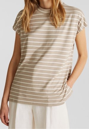 Woman wearing a beige and white horizontal striped short-sleeve top with hand in pocket and white loose pants.