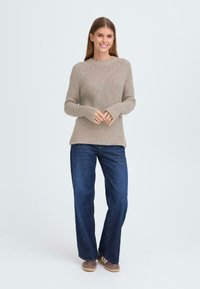 Beige strikket genser med ribbet tekstur, rund hals og lange ermer, paret med mørkeblå vide jeans og brune sko.