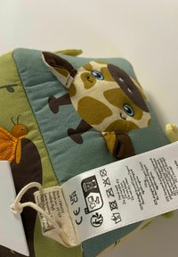 Puha, steppelt textil játék zsiráf mintával; különböző textúrákkal, földszínekkel és gondozási utasításokat és szimbólumokat tartalmazó címkével.