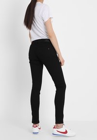 Jeans negros ajustados de cintura alta, combinados con una camisa blanca de manga corta y zapatillas rojas y blancas. Textura suave y diseño ceñido.