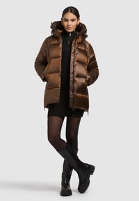 Brūna pūdera jaka ar kapuci, ar šūtu rakstu un priekšējo rāvējslēdzēju. Valkāta virs melnas ribotas kleitas un kombinēta ar melniem pusgarajiem zābakiem.