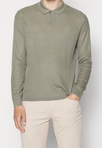 Long-sleeve polo shirt in olive green, featuring a textured knit pattern, classic collar, and ribbed cuffs and hem. Casual fit.