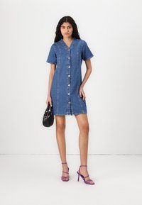 Denim-mekko lyhyillä hihoilla, etunapeilla ja suoralinjaisella siluetilla. Ominaisuuksia ovat vaaleansininen pesu ja ommellut yksityiskohdat.