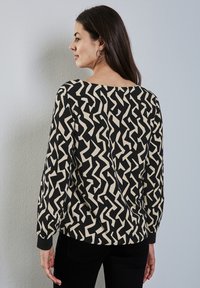 Blusa de manga larga en un patrón abstracto en negro y beige, con un escote amplio y un diseño corto con puños ajustados.