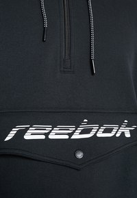 Svart sweatshirts med kvartdragkedja, med texturerat tyg, vit "reebok"-logotyp över framsidan och kontrasterande snörning.