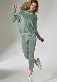 Mintgroene velours trainingsoutfit met een loszittend capuchon sweatshirt en tapered broek. Witte sneakers. Gladde textuur, ontspannen ontwerp.