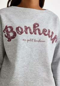 Grå sweatshirt med oversized bordeaux tekst "Bonheur" med tekstureret finish og mindre tekst nedenfor, lavet af blødt bomuldsstof.