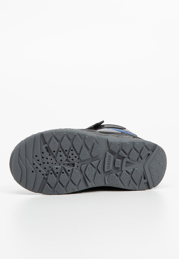 Czarna podeszwa buta z teksturowanym, gumowym wzorem z sześciokątnymi i okrągłymi kształtami. Zawiera otwory drenażowe i szczegóły logo.