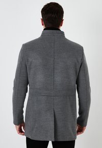 Grijze, middelange jas met een hoge kraag, rechte snit en textuurstof, voorzien van een achterkant met split en subtiele stikdetails.