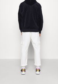 Schwarzer Fleece-Hoodie, weiße Cargo-Hosen mit seitlichen Taschen und Sneaker mit schwarzen, weißen und neonfarbenen Akzenten. Lockere Passform.
