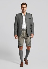 Veste en laine grise avec des accents verts, chemise blanche, shorts gris brodés, chaussettes grises jusqu'aux genoux et chaussures en cuir marron.