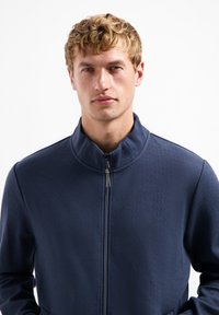 Marine zip-up jack met een gestructureerd visgraatpatroon, hoge kraag en zakken aan de voorkant. Gemaakt van een zachte, lichte stof.