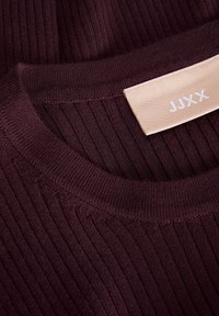 Col montant en maille côtelée bordeaux avec une étiquette en tissu beige cousue à l'intérieur affichant les initiales de la marque JJXX.