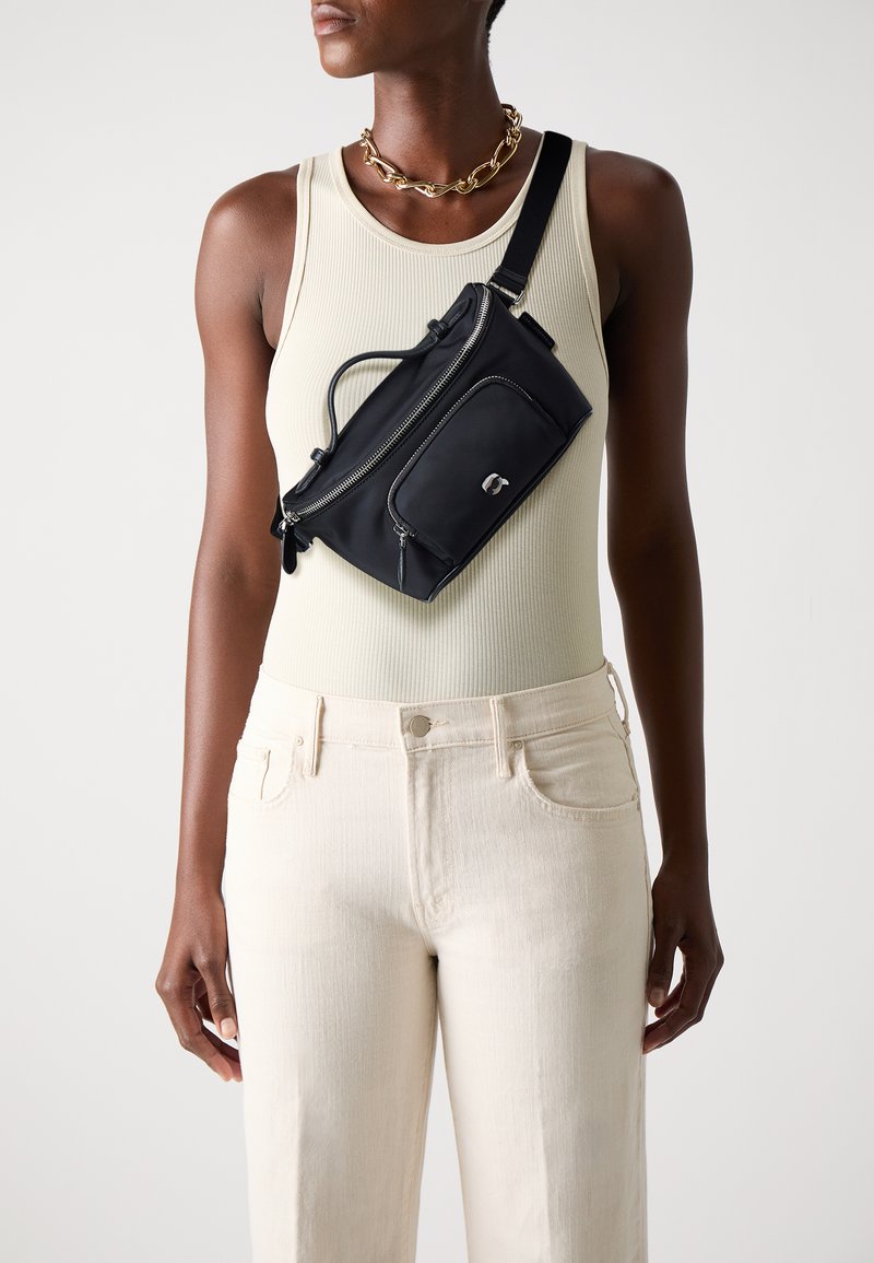 Black nylon crossbody bag with zippered pockets, featuring a top handle and adjustable strap, styled against a light-colored top and pants.