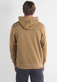 Sweat à capuche marron en tissu texturé, avec un design simple et des détails de couture, vu de dos.