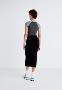 Haut ajusté gris et teal à manches courtes associé à une jupe crayon noire mi-longue. Porté avec des chaussettes blanches et des chaussures de sport.