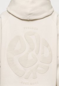 Sudadera con capucha blanca con logo grande texturizado y la palabra "PEGADOR" en relieve encima. El material parece suave y liso, con un diseño casual.