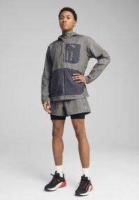 Grå och marinblå vindjacka med en dragkedjeficka, bärs över en matchande grå shorts-set. Inkluderar svarta och röda löparskor med vita accenter.
