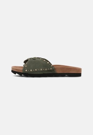 Sandalia plana tipo chancla con parte superior de ante verde oscuro con tachuelas y suela acolchada color camel sobre suela exterior negra con dibujo antideslizante, mostrada de perfil.
