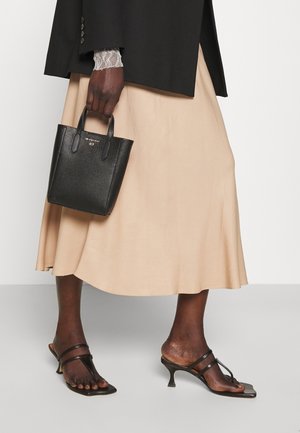 Sac cabas en cuir noir texturé avec des poignées courtes, associé à une jupe beige fluide et des sandales à talons noires à lanières.