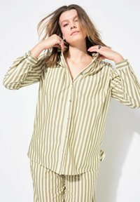Camisa de botones a rayas en verde oliva y crema, con cuello, dos bolsillos frontales y una tela suave con un ajuste relajado.