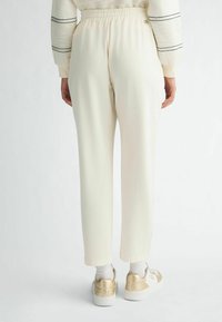 Pantalons couleur crème avec une coupe décontractée, dotés d'une taille élastique et d'ourlets retroussés, associés à des baskets ornées de détails dorés.