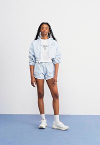 Light blue cropped hoodie with drawstrings, matching shorts, and white t-shirt featuring an outline graphic. White sneakers complete the outfit.