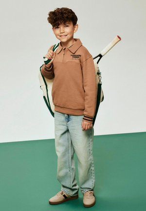 Brūns garām piedurknēm polo krekls ar uzrakstu "Tournament Tennis", gaisīgi zili džinsi, bēšas sporta kurpes, rokā tenisa rakete un divtónu soma.