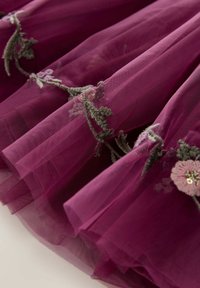 Tulle bordeaux avec broderies florales en vert et rose. Conception superposée avec une texture douce et de délicats accents de perles sur les fleurs.