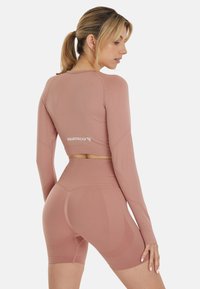 Roze langmouw cropped top met een ronde hals en logodetail, gecombineerd met high-waisted shorts met textuuraccenten.