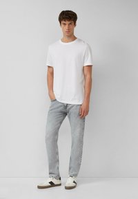 Biała bawełniana koszulka w połączeniu z jasnoszarymi dżinsami i białymi trampkami z czarnymi akcentami. Prosty design, casualowy krój.