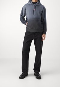 Felpa con cappuccio in gradiente blu-grigio con tasca a canguro frontale e logo. Abbinata a jeans neri a gamba dritta e scarpe nere.