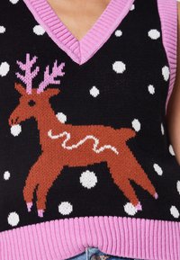 Gilet en maille noire avec des pois blancs comme des flocons de neige, bordure rose, et un renne marron avec des bois et des sabots roses, portant une écharpe blanche ondulée.