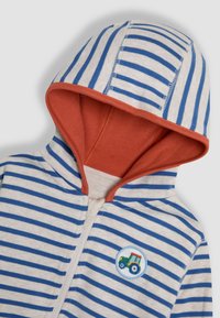 Leichtgewichtiger Hoodie mit gestreiftem Muster in Creme mit blauen Streifen, rotem Innenfutter und einer runden Traktor-Applikation auf der Brust. Zip-Verschluss vorne.