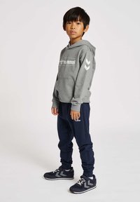 Grauer Kapuzenpullover mit weißem Logo, marineblaue Jogginghosen und marineblaue Sneakers mit weißen Akzenten und Riemen. Verfügt über einen lässigen Schnitt und weiche Materialien.