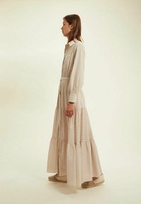 Robe longue rayée avec un devant à boutons et une taille ceinturée. Présente une jupe en couches en tissu doux et léger, avec des manches longues et un col.