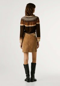 Maglione marrone con motivo zigzag arancione e crema, abbinato a una gonna in cordoncino beige. La modella indossa stivali neri con tacco al ginocchio.