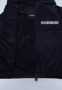 Marineblå jakke med mesh-fôr, glidelåslukking og et fremtredende logo på brystet. Glatt ytterstoff med elastiske mansjetter og nederkant.