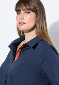 Navyblauwe overhemdo met een puntkraag en een verticale roodgestreepte accent bij de halslijn. Soepele textuur met een ontspannen pasvorm.