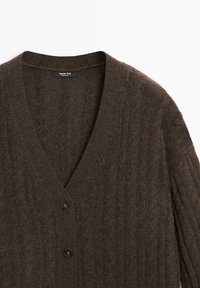 Bruine gebreide cardigan met V-hals, geribbelde textuur en drie zwarte knopen aan de voorkant. Gemaakt van zacht, dik garen.