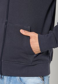Marine blauwe zip-up hoodie van zachte stof, met zijzakken en geribbelde manchetten. Vrij losse pasvorm met zichtbare stikseldetails.