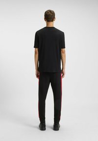T-shirt nero a maniche corte abbinato a pantaloni neri con strisce rosse sui lati. Il tessuto appare liscio con una vestibilità comoda.